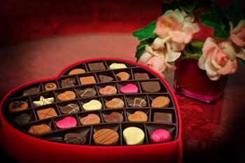 Photo of a box of chocolates next to vase of flowers